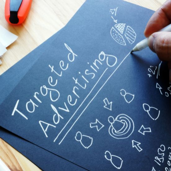 A person draws the words "targeted advertising" on a small hand held chalk board.